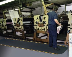 Man standing on a Hog Heaven anti fatigue mat runner with Yellow Striped border in a 7/8" floor mat thickness in front of a printing press