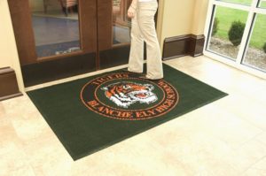 Waterhog Inlay custom logo mat with fashion borders with man walking over the mat at a high school entrance