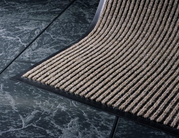 Close up corner view of Dual Rib Walk off matting in a beige color showing the smooth vinyl edges and ribbed surface pattern
